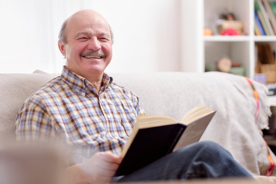 Senior Man Reading A Book On His Sofa