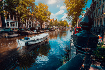 Naklejka premium Kanał w Amsterdamie w jesiennym słońcu. Łódka pływająca wzdłuż drzewa, żywe odbicia, białe chmury na niebie. Holandia domy krajobraz punkt orientacyjny