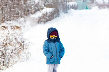 Fototapeta na wymiar A boy in sunglasses and a blue jacket on a snowy slope.