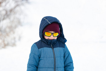 Fototapeta na wymiar A boy in sunglasses and a blue jacket on a snowy slope.
