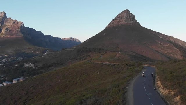 aerial view of a single tour motorcyclist during sunrise on signal hill, Cape Town, with table mountain and lions head