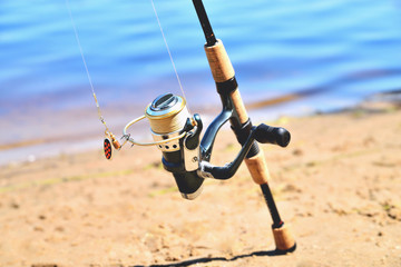 fishing rod with reel on the background of the river, blue water, sun, sand
