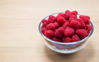 glass bowl full of ripe juicy raspberries isolated on a wooden counter with copy space