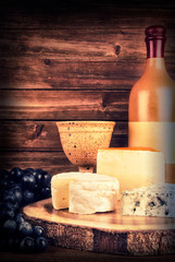 Bottle and glass of wine isolated on a wooden plank in background. Set of cheese on table.
