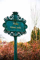 Street sign in Paris, France. Avenue Pierre-Loti is an alley of Champ de Mars. Typical vintage pointer signpost and spring trees at background. Traditional parisian plaque with the name of the alley.