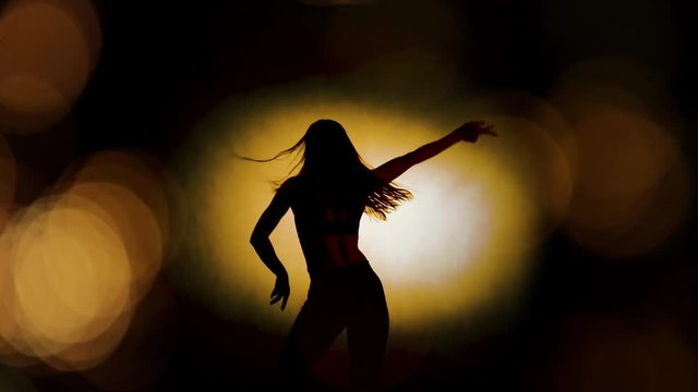 Female shadow dancer silhouetted dancing against an abstract background of lights with lens flares and bokeh effect