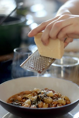 Grating parmesan cheese on a plate of mistrone soup with pasta, beans and vegetables. Selective focus.
