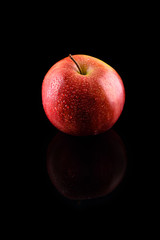 Fototapeta na wymiar Ripe red apple with water drops on a black background with refle