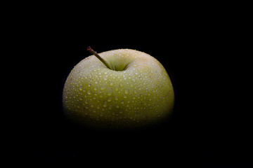 Top of a green ripe apple in drops of water on a black backgroun