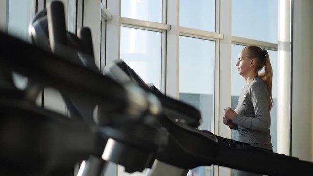 Attractive woman of middle age is running on tread mill in sport gym