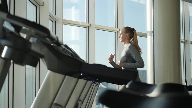 Attractive woman of middle age is running on tread mill in sport gym