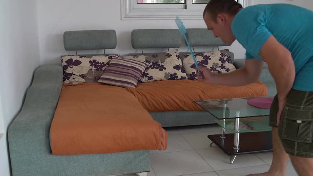 A man tries to kill a fly on the sofa with a fly swatter but misses