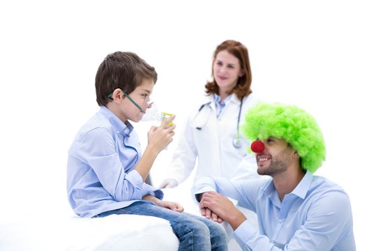 Boy using nebuliser with doctor dressed as clown