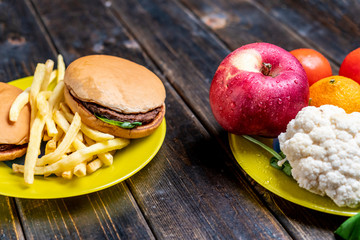 junk food or healthy vegetables and fruits on dark wooden table isolated b