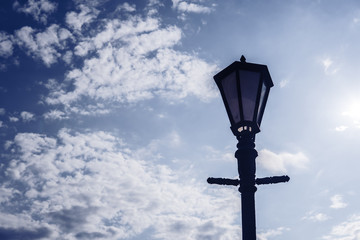 An old lamp post with the lantern back lit by the sun against a blue sky
