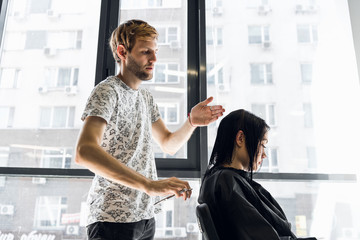 Obraz premium Young beautiful woman having her hair cut at the hairdresser's. Young male hairdresser smiling and making hairstyle to the customer.