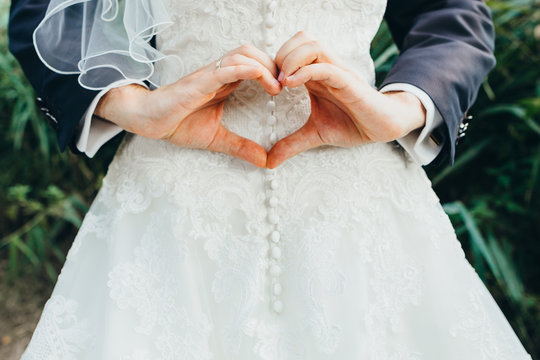 Br&auml;utigam formt Herz aus Fingern mit Hochzeitskleid im Hintergrund