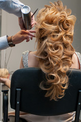 Fototapeta premium Process of creating evening hairstyles for a girl with long blond hair by a master hairdresser at a beauty marathon in Chelyabinsk, Hotel Redisson Blue, December 2, 2018