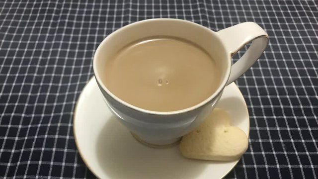 Cinemagraph - Steaming white cup of coffee with heart shaped cookie on a table with a checkered tablecloth