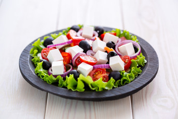Greek salad with fresh vegetables on wooden background, feta cheese and black olives. Love for healthy raw food concept.