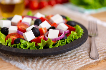Greek salad with fresh vegetables on wooden background, feta cheese and black olives. Love for healthy raw food concept.