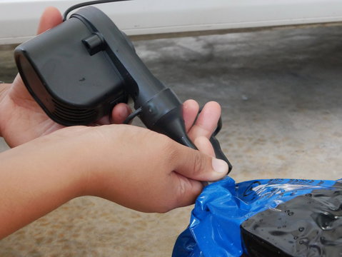 A woman's hands holding and using mini air pump, connected to the car plug, to inflate a rocking doll