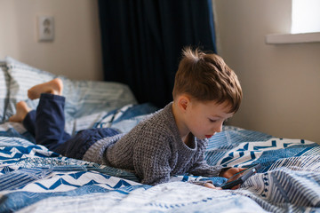 Toddler boy is lying looking at the phone. The concept of dependence on gadgets