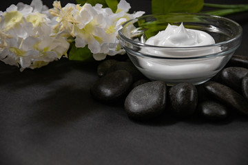 Fototapeta na wymiar side view of natural skin care ointment in glass bowl on rock base with bouquet of white lilacs.
