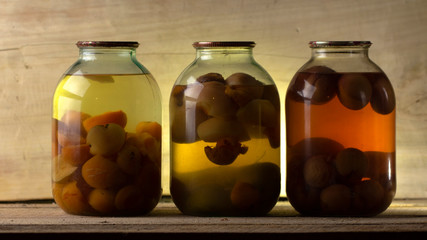 Several cans of compote on a wooden shelf in a dark basement