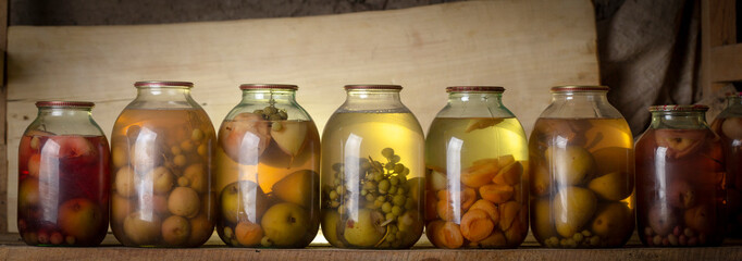 Several cans of compote on a wooden shelf in a dark basement