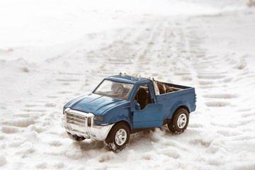 Fototapeta na wymiar Toy blue pickup car in winter forest. Stands on the road. In the back of pickup truck are Christmas tree cones.