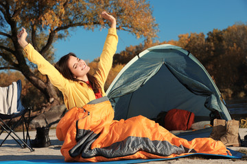 Woman waking up in sleeping bag near tent outdoors