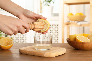 Woman squeezing lemon juice with wooden reamer into glass bowl at table