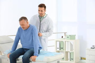 Doctor examining mature patient with stethoscope in hospital. Space for text