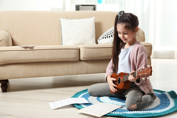Cute little girl playing guitar on floor in room. Space for text