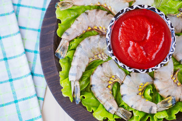 Raw tiger shrimp headless on a wooden plate with sauce. Ingredients for cooking.View from above. - obrazy, fototapety, plakaty