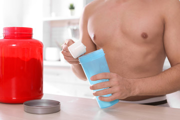 Obraz na płótnie Canvas Young shirtless man preparing protein shake at table in kitchen, closeup