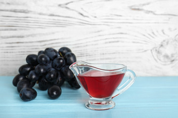 Glass gravy boat with wine vinegar and fresh grapes on wooden table