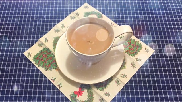 Cinemagraph - Animated snow falling on the white cup of coffee with heart shaped cookie on a table with a checkered tablecloth. Christmas breakfast. Holiday still life. Top view