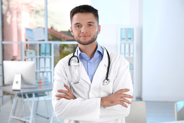 Young male doctor with stethoscope wearing white coat in clinic