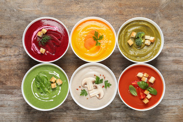 Various cream soups in bowls on wooden background, top view