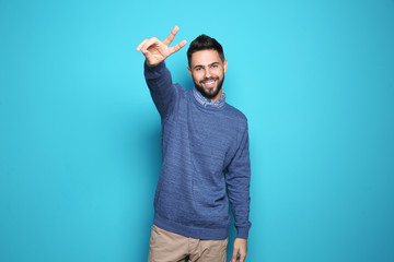 Happy young man showing victory gesture on color background