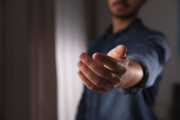 Man offering helping hand on blurred background, closeup. Space for text