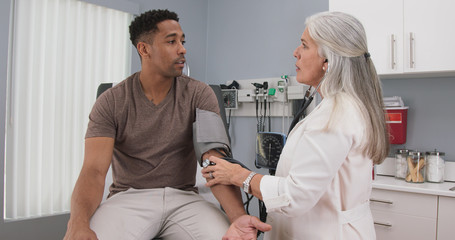 Portrait of young male patient having blood pressure measured by mature medical doctor. Close view of doctor measuring blood pressure of black male indoors health clinic