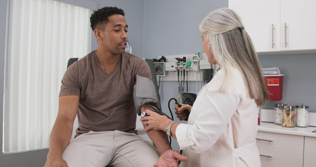 Obraz premium Portrait of young male patient having blood pressure measured by mature medical doctor. Close view of doctor measuring blood pressure of black male indoors health clinic