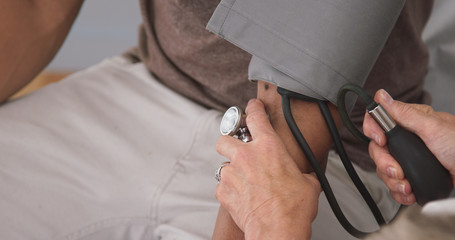 Close up of doctor pumping gauge to measure patients blood pressure. Tight shot of senior doctor measuring blood pressure of young black male