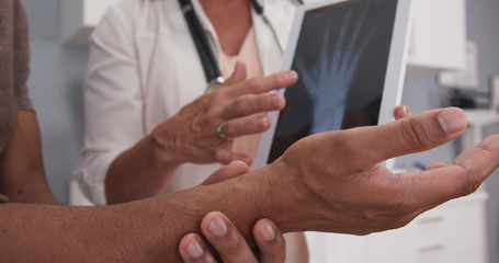 Close up of male patient hand and wrist with doctor explaining x ray on tablet. Tight view of senior doctor holding electronic pad with x-ray of patients wrist and hand