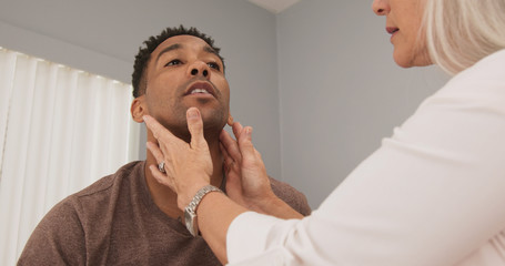Mature female doctor checking male patients neck for swollen thyroid or lymph nodes. Senior doctor...