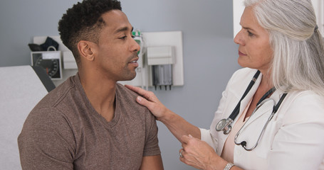 Close up of senior female doctor examining male patients neck. Portrait of attractive black male having doctor checkup at health clinic