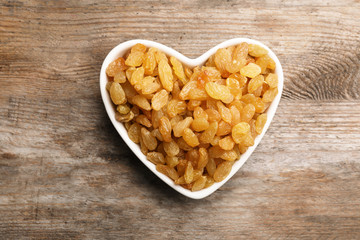 Heart shaped plate with raisins on wooden background, top view. Dried fruit as healthy snack